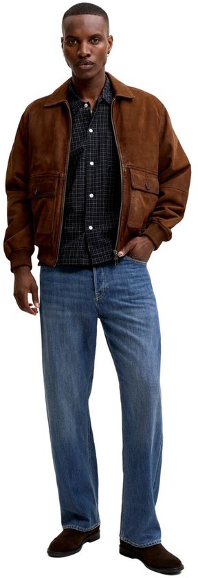 Man met bruine jas, geruite blouse en rechte blauwe jeans, staand.