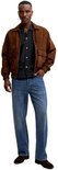 Man met bruine jas, geruite blouse en rechte blauwe jeans, staand.