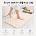 Een beige badmat met een gedempt geometrisch patroon, gezien vanuit een laag perspectief met een voet die erop stapt.