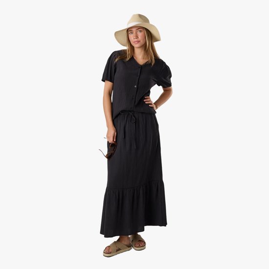 Model in zwarte blouse, lange geruite rok met strikceintuur, strooien hoed, zonnebril en sandalen.