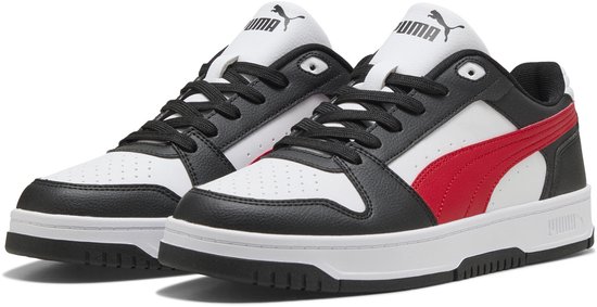 Paar witte Puma sneakers met zwarte en rode strepen, witte zolen.
