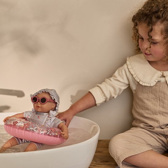 Meisje met een pop met gestreept zwempak, zwemband en zonnebril in een badje.