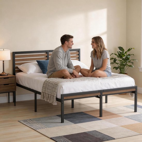 Man en vrouw zittend op een tweepersoonsbed met zwart metalen frame en houten accenten, in een lichte kamer.