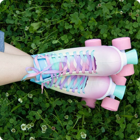 Roller skates met pastelkleurige gradiënt en paarse, roze, blauwe veters, gedragen in het gras.