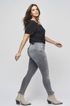Vrouw in grijze skinny jeans met rafelende zoom en zwarte t-shirt.