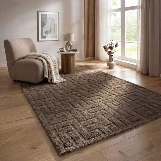 Tapis marron à motif géométrique dans un salon avec fauteuil, petite table et vase.