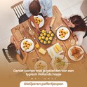 Een familie aan tafel eet poffertjes uit een gietijzeren poffertjespan. Gekookte maiskolven en brood liggen op tafel.