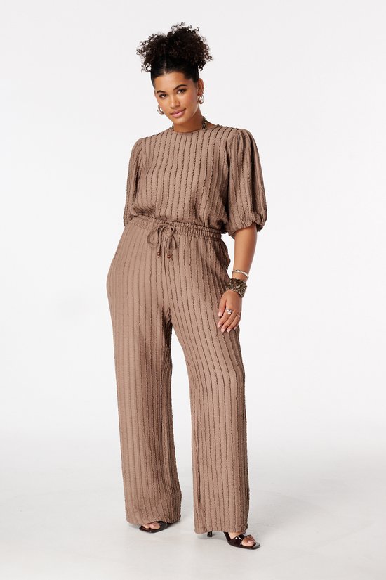 Model met bruine jumpsuit, met verticale plooien, trekkoord en pofmouwen.