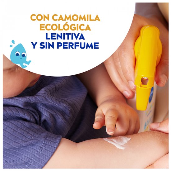 Hand houdt een babyarm vast. Witte crème wordt op de babyarm gesmeerd met een gele sprayflacon op de achtergrond.