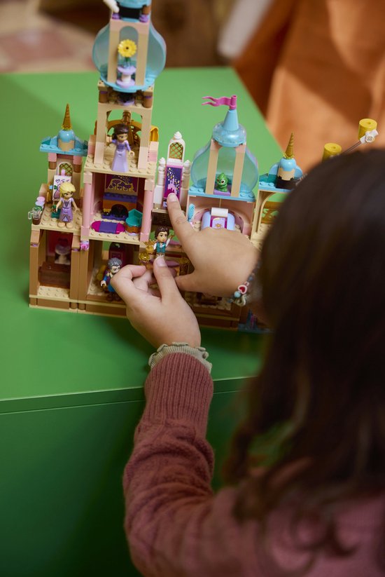 Meisje in roze vest wijst naar LEGO kasteel met figuurtjes en blauwe torens.