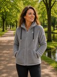Een vrouw met bruin haar, lachend, draagt een grijze fleece hoodie met zwarte trekkoorden in een park.