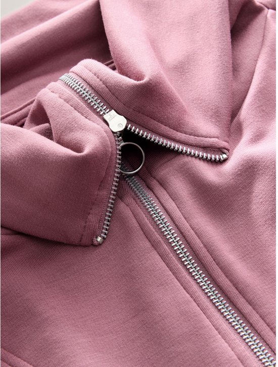 Gedetailleerde close-up van de korte zilverkleurige ritssluiting met ringtrekker op de roze sweater.