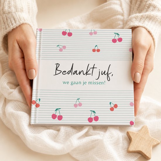 Een afscheidsboekje met de tekst 'Bedankt juf, we gaan je missen!' op een mintgroene gestreepte achtergrond met kersen. Vastgehouden door handen.