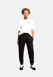 Model draagt een zwarte Puma joggingbroek met elastische tailleband en logo op linkerbeen.