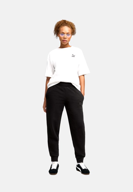 Model draagt een zwarte Puma joggingbroek met elastische tailleband en logo op linkerbeen.