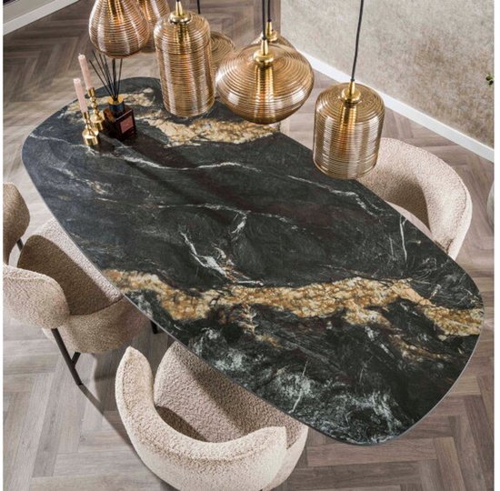 Ovale eettafel met een zwart marmerlook keramiek blad met gouden aders, omringd door beige bouclé stoelen.