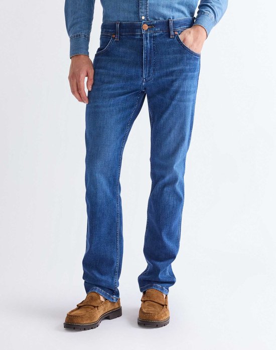 Man in blauwe Wrangler jeans en spijkerhemd, met een hand in de zak.