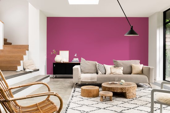Een woonkamer met een fuchsia muur, stoffen bank, houten salontafel en rotan stoel.