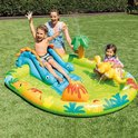 Een gezin geniet van een opblaasbaar dinosauruszwembad met glijbaan en fontein in de tuin.