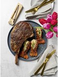 Tomahawk steak met kreeftstaarten op een bord, met tulpen en een Meater+ thermometer in houten houder.