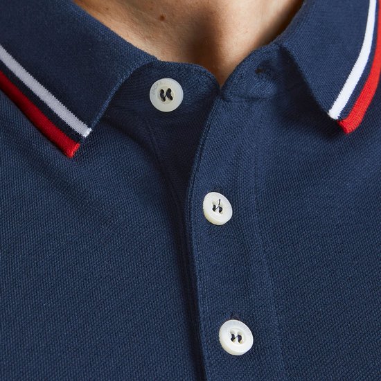 Detail van de kraag van een donkerblauwe polo met rode en witte strepen en witte knopen.