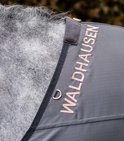 Close-up van een grijze paardendeken met de tekst "WALDHAUSEN" in koperkleurige letters.