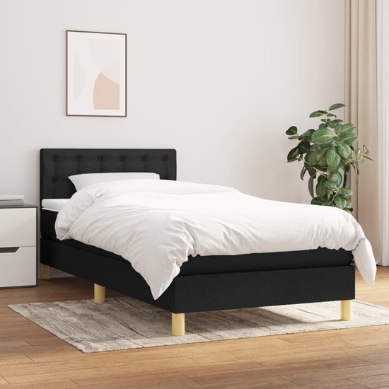 Lit boxspring noir avec tête de lit rembourrée et couettes blanches, dans une chambre.
