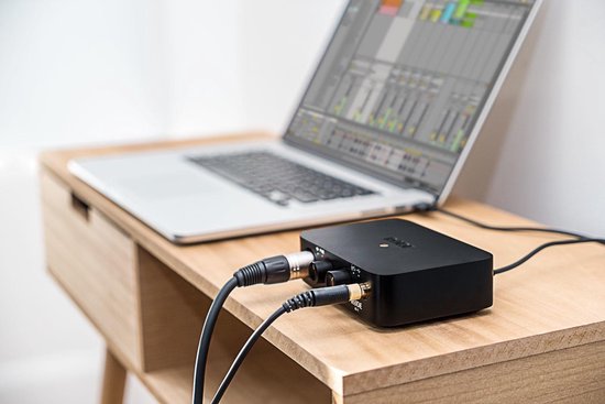 Zwarte RØDE AI-1 audio interface, aangesloten op een laptop en microfoon, op een houten bureau.
