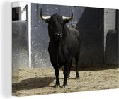 Un taureau noir sur le sable devant une porte 120x80 cm - Tirage photo sur toile (Décoration murale salon / chambre)