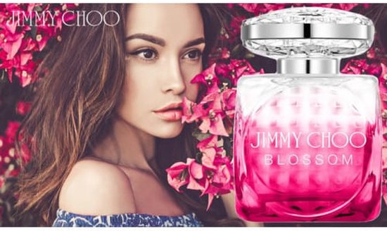 Vrouw naast een fles Jimmy Choo Blossom parfum tegen een achtergrond van roze bloemen.