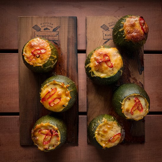 Zes ronde courgettes, gevuld met kaas en chilipepers, op twee cederhouten planken.