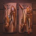 Vier gegrilde vissen op cederhouten planken, met bruine en gele tinten en een gestreepte buik.