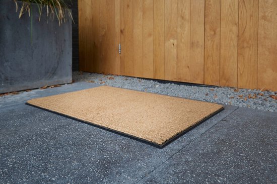Kokosdeurmat met zwarte rand op een betonnen ondergrond, naast een houten deur.