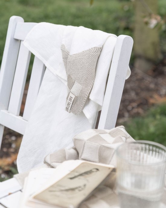 Witte linnen theedoek met een beige gebreide hoek met ruitpatroon op een witte stoel.