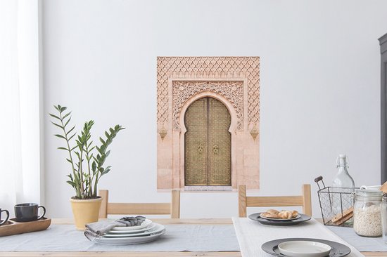 Une porte marocaine couleur sable avec des détails dorés et une sculpture sur pierre complexe, accrochée au-dessus d'une table à manger.