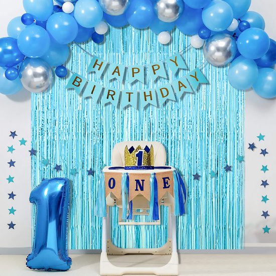 Kinderstoel met 'ONE' banner voor een lichtblauw folie gordijn, met ballonnen en sterdecoraties, en een grote blauwe '1' ballon.