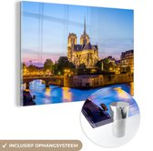 MuchoWow® Glasschilderij 30x20 cm - Schilderij acrylglas - Een verlicht Notre Dame met blauw water ervoor in Frankrijk - Foto op glas - Schilderijen