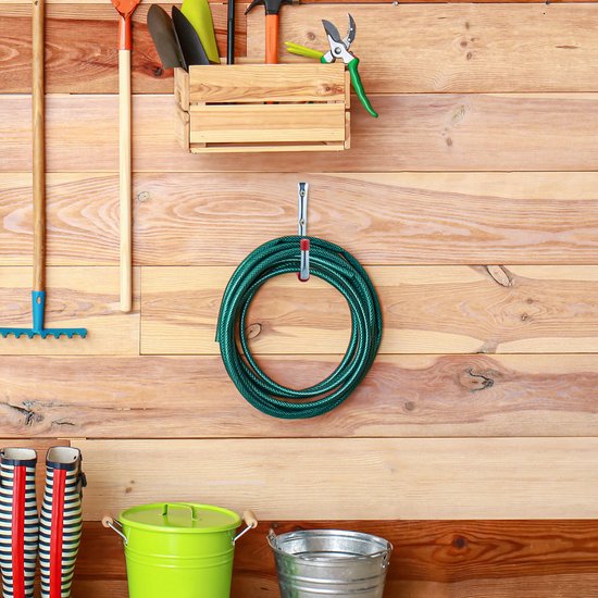 Tuimgereedschap hangt aan een houten muur, waaronder een groene tuinslang.