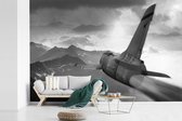 Behang - Fotobehang Een straaljager van een leger over de bergen - zwart wit - Breedte 390 cm x hoogte 260 cm