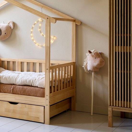 Een houten stokpaardje met een lichtbruin hoofd en witte manen, naast een houten bed.