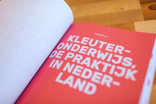 Open boekpagina met rode kaft, met de tekst 'KLEUTERONDERWIJS, DE PRAKTIJK IN NEDERLAND'.