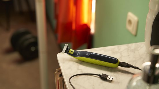 Felgroen en zwart Philips OneBlade scheerapparaat met USB-kabel op een marmeren tafel.