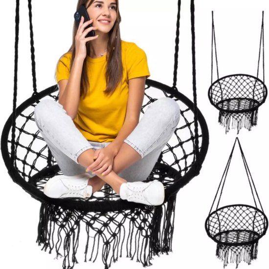 Zwarte macramé hangstoel met franjes, een vrouw in een gele top zit erin, telefonerend.