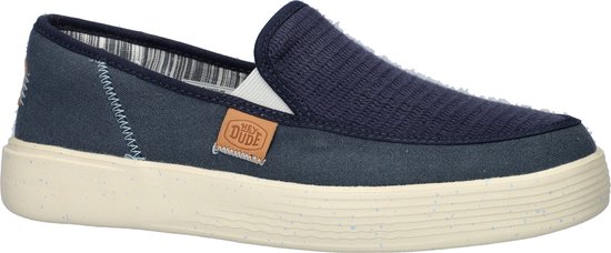 Mocassin HEYDUDE bleu en textile avec une semelle blanche. Le côté a une étiquette marron avec logo.
