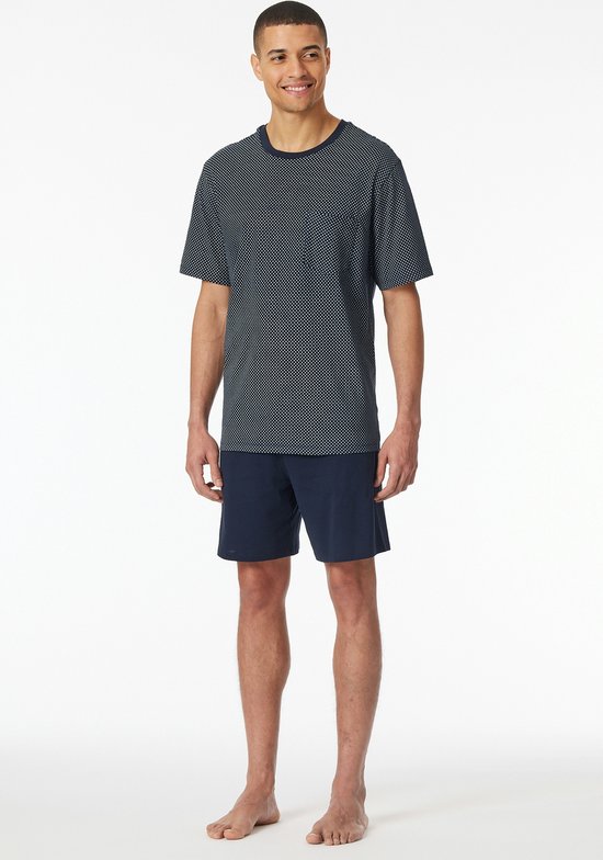 Man in nachtblauw pyjamashort met donkerblauw, wit geprint t-shirt met kleine ruitjes.
