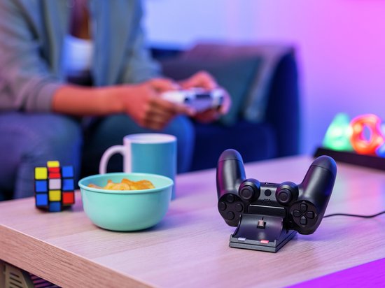 Close-up van een zwarte laaddock met een PlayStation 4 controller erop geplaatst, in een woonkamer met neonverlichting.