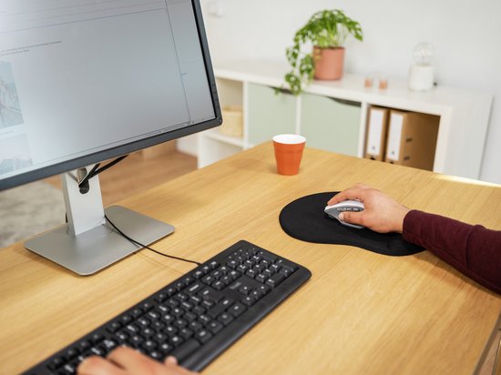 Tapis de souris noir avec repose-poignet, avec une souris et une main dessus, sur un bureau en bois.