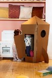 Twee kinderen kruipen in een kartonnen raket in een kamer.