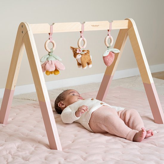 Baby ligt onder houten babygym met speeltjes: bloem, hertje en aardbei.