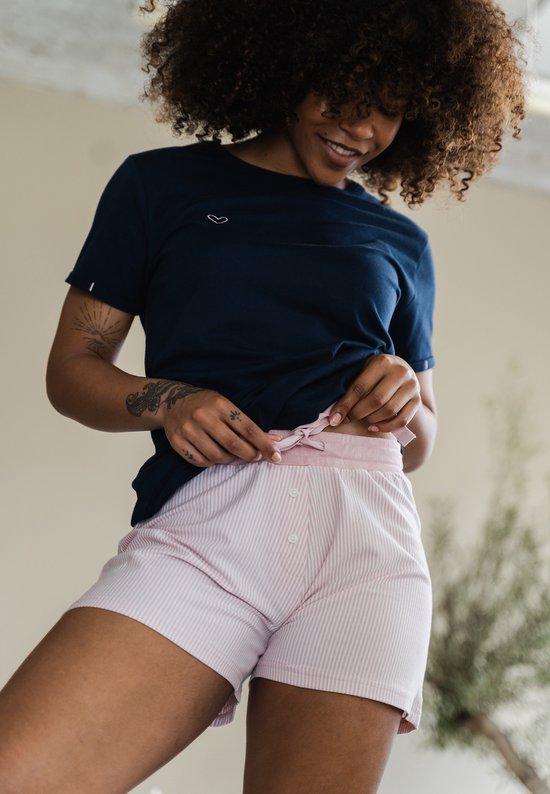 Model draagt een donkerblauwe pyjamatop met een klein hartje en een roze gestreepte pyjamashort met strik.